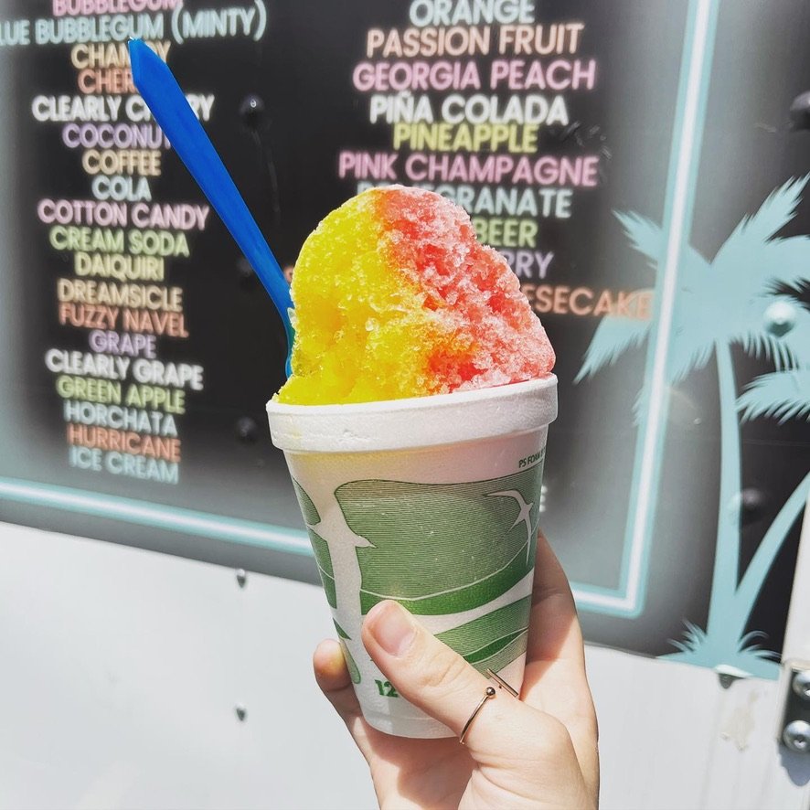 A colorful shaved ice cup held in front of the menu board
