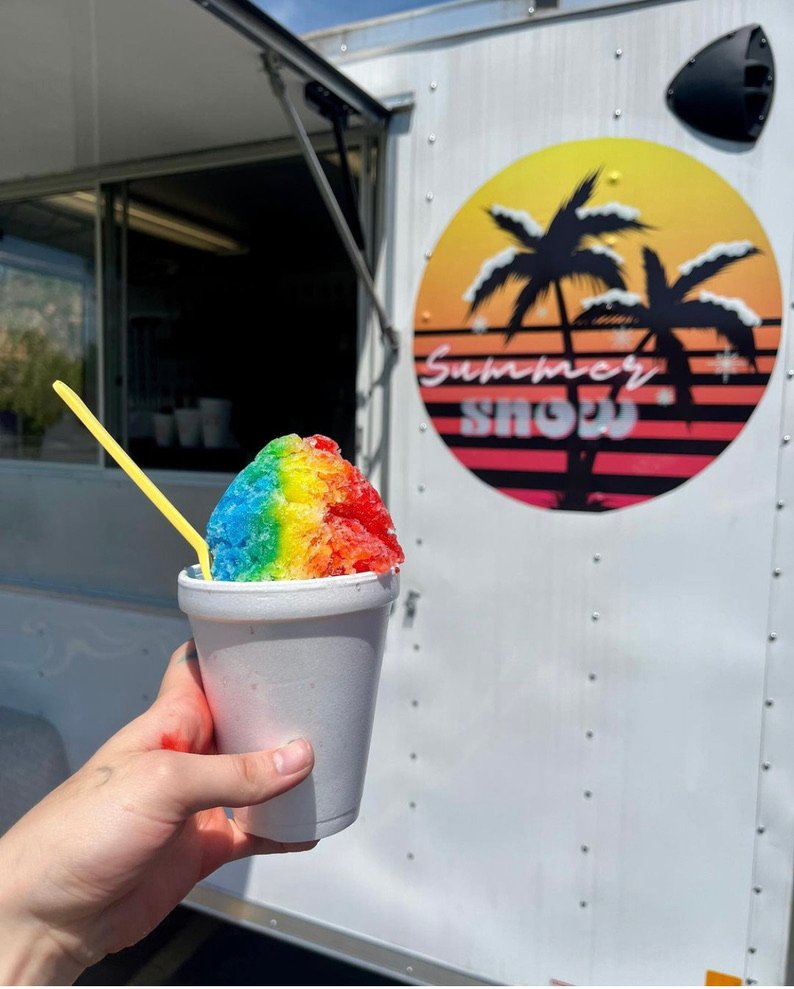 A rainbow shaved ice cup in front of the Summer Snow trailer